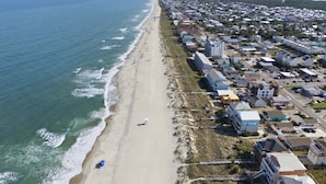 Vista aerea di una località costiera con spiaggia, edifici residenziali e cielo sereno.