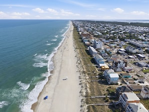 An aerial view of a coastal town with a beach, residential buildings, and a clear sky.