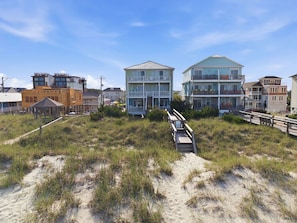 Una propiedad frente a la playa con un paseo marítimo de madera que conduce a un edificio de varios pisos con balcones.