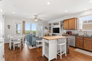 A modern kitchen with white cabinetry, a wooden island, and a dining area with a blue sofa.