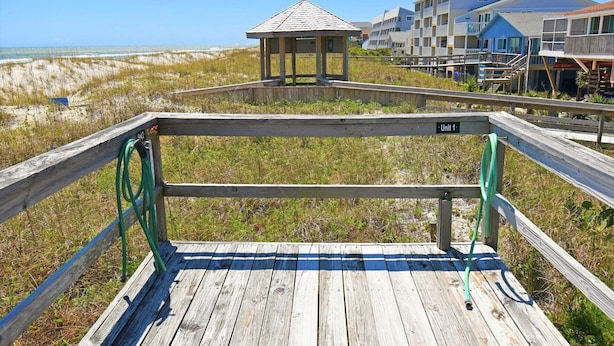 Una passerella in legno che conduce a una spiaggia, con un gazebo e un edificio a più piani sullo sfondo.