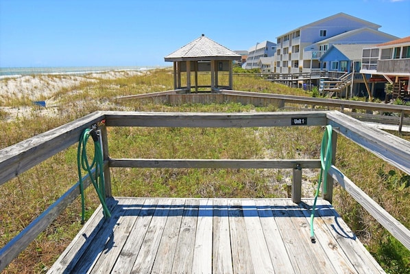 A wooden boardwalk leading to a beach area with a gazebo and a multi-story building in the background.