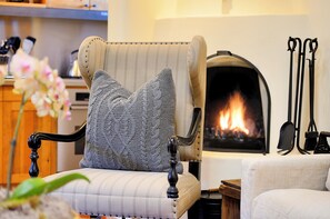Una silla con un cojín tejido, una chimenea y una mesa de madera en una habitación acogedora.