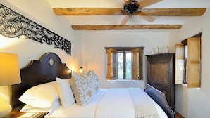 A bedroom with a bed, wooden headboard, a nightstand, a lamp, a ceiling fan, and a window with wooden shutters.