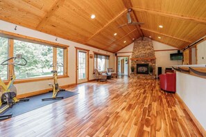 A spacious room with wooden flooring, a stone fireplace, and exercise equipment. - Holbrook Retreat - 5 bedroom on 47 acres (Detroit Lakes)