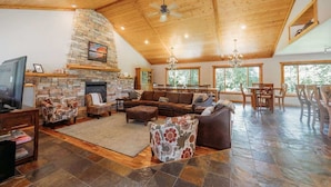A spacious living room with a stone fireplace, wooden ceiling, and large windows. - Holbrook Retreat - 5 bedroom on 47 acres (Detroit Lakes)