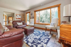 A living room with leather sofas, a patterned rug, and large windows with wooden frames. - Holbrook Retreat - 5 bedroom on 47 acres (Detroit Lakes)