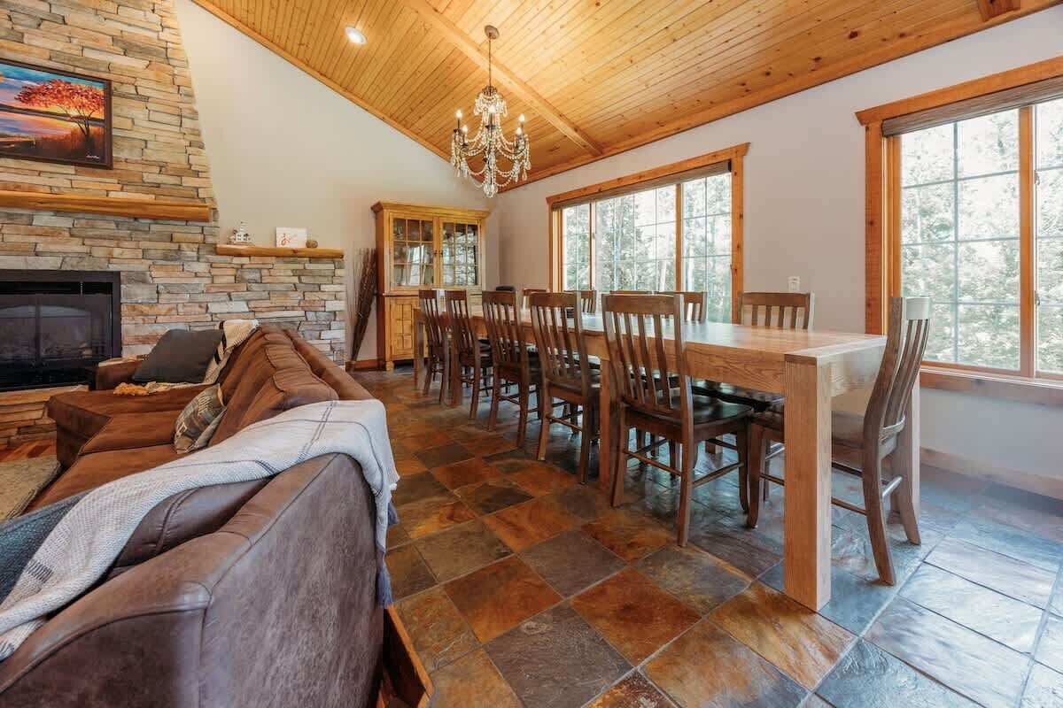 A spacious living area with a fireplace, a dining table with chairs, and large windows.