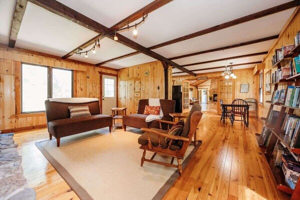 A wooden interior with a sofa, chairs, a dining table, and a bookshelf.