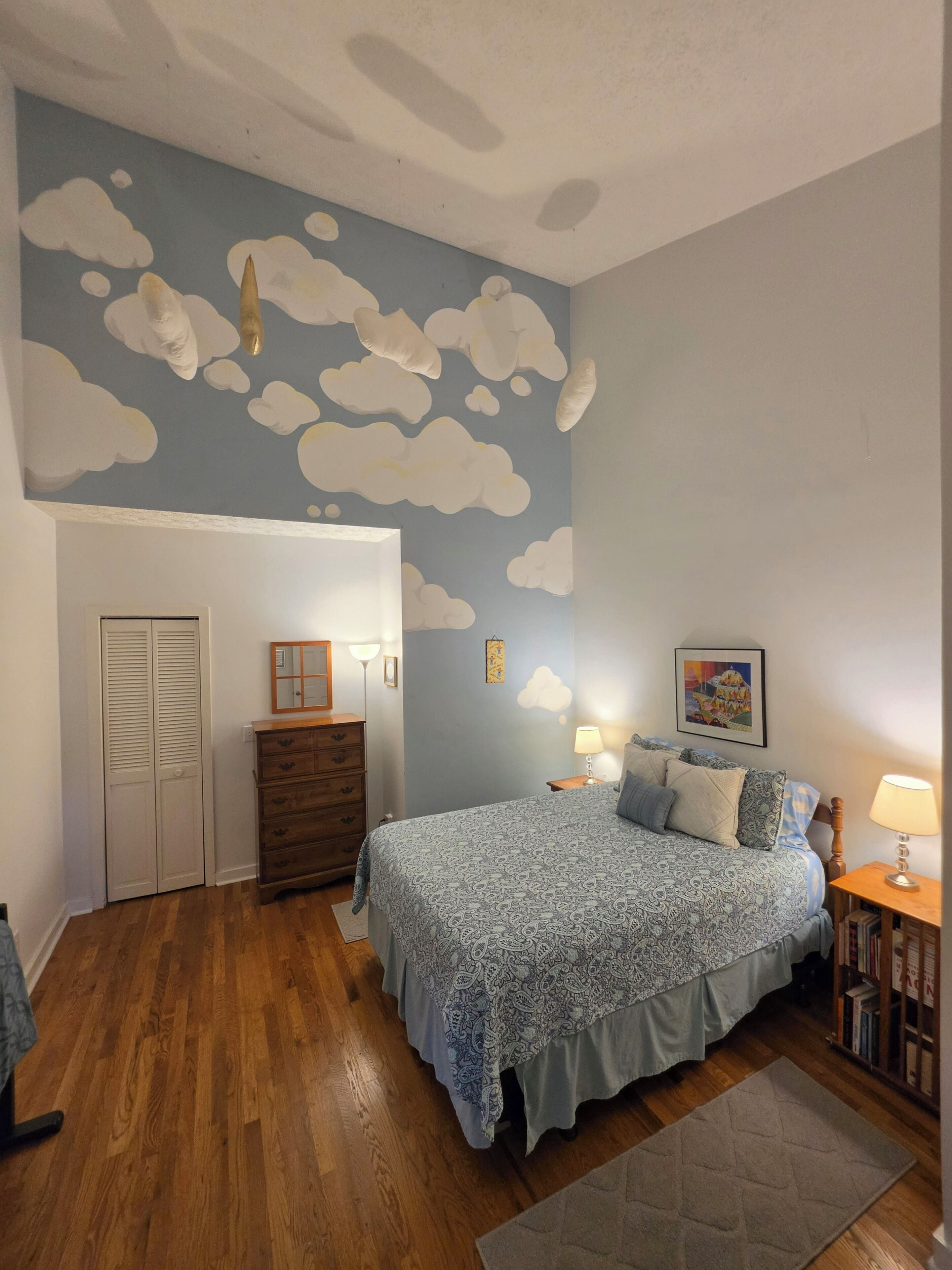 A bedroom with a bed, dresser, and a wall with cloud decorations.