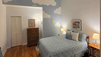 A bedroom with a bed, dresser, and a wall with cloud decorations.