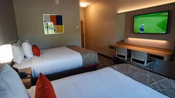 Habitación de hotel con dos camas, un televisor mostrando un partido de golf, un escritorio con sillas y un televisor montado en la pared.