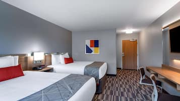 A hotel room with two beds, a desk, a chair, and a TV.