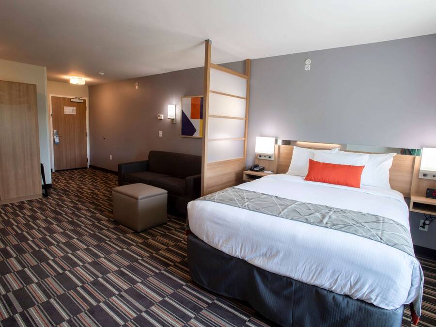 Una habitación de hotel con una cama grande, un escritorio, una silla, un armario y una pequeña cocina.