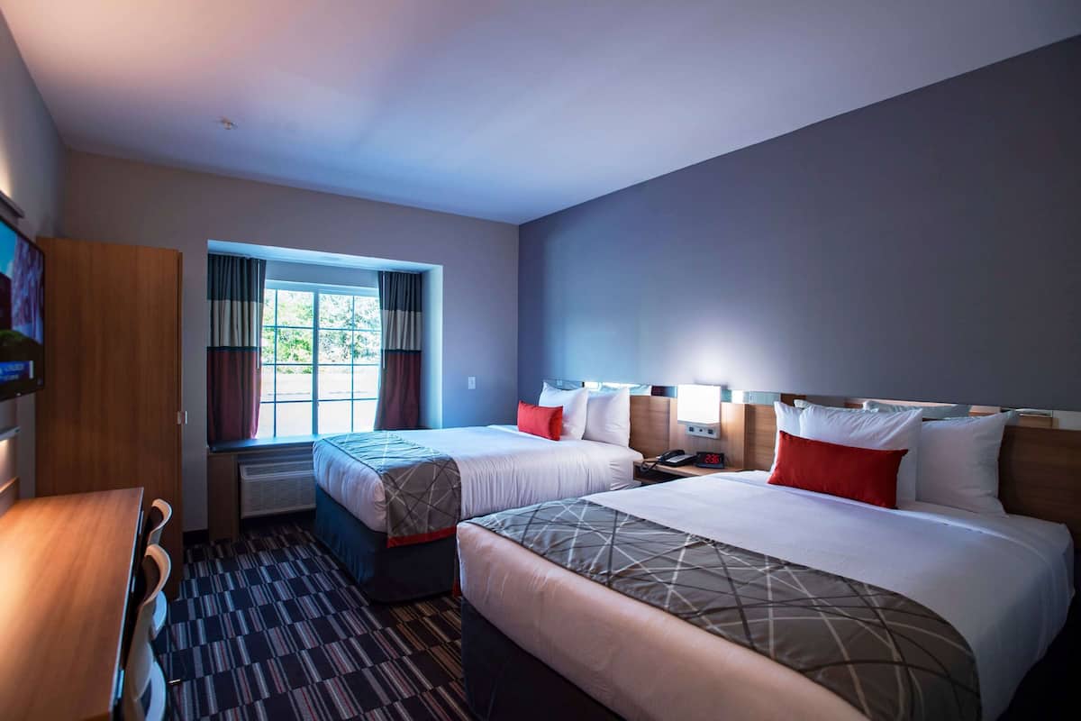 A hotel room with two beds, a desk, a window with curtains, and a wooden wardrobe.