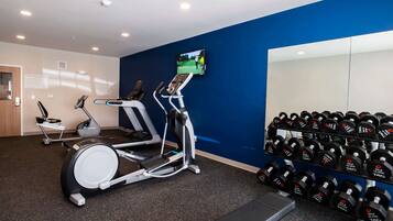 A gym with exercise equipment, a television, and a rack of dumbbells.