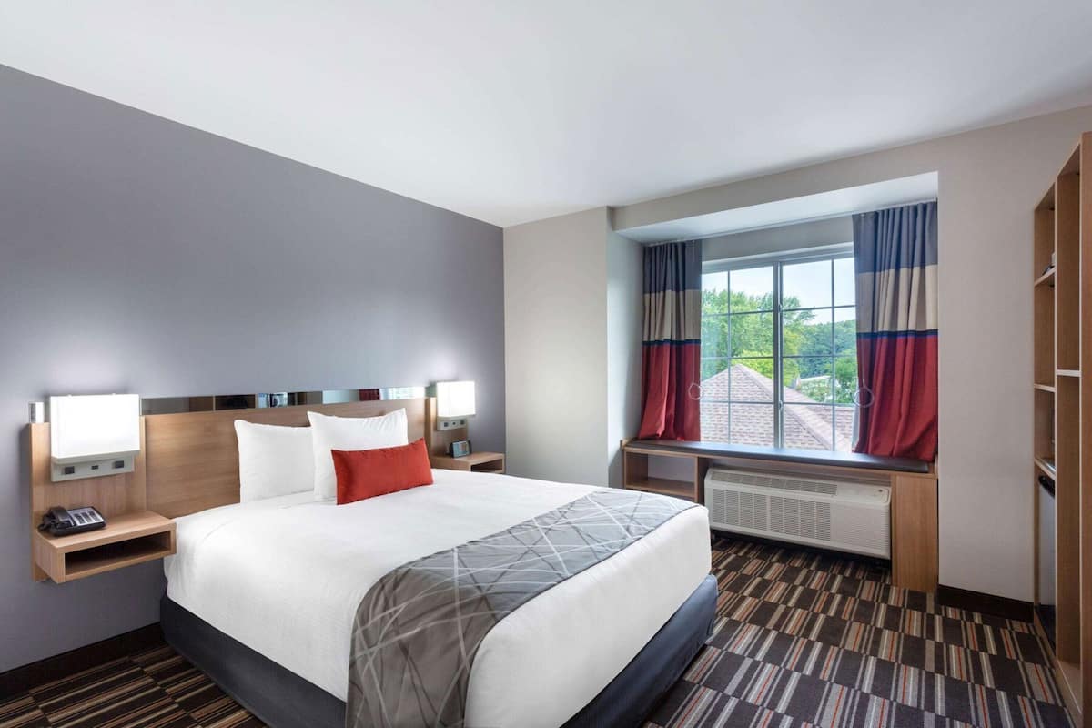 A hotel room with a large bed, bedside lamps, a window with curtains, a radiator, and a wooden wardrobe.