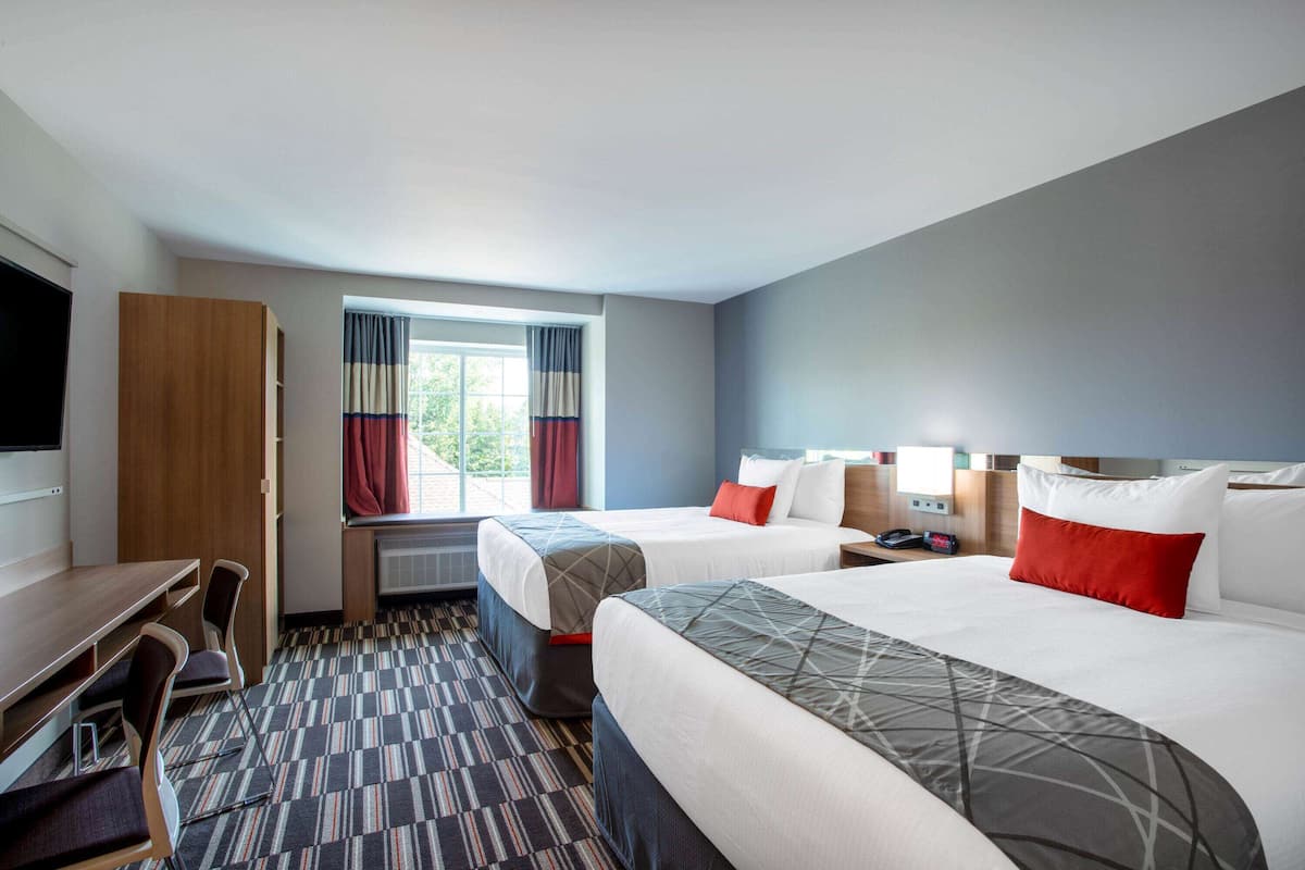 A hotel room with two beds, a desk, a wardrobe, and a window with curtains.