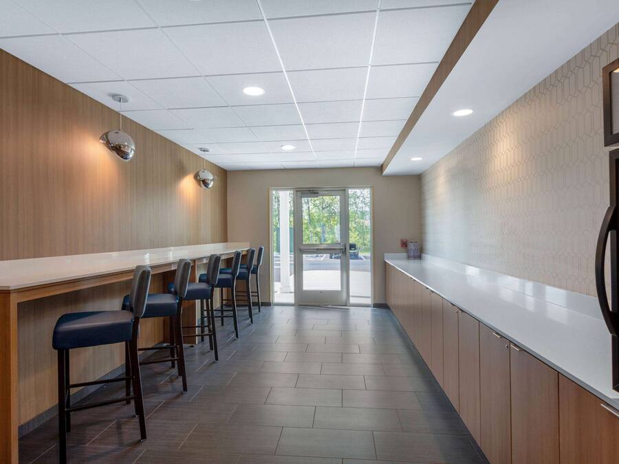 A modern kitchen with a long counter, bar stools, and a view through the glass door.