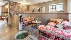 Una sala de estar acogedora con una pared de piedra, sofás con estampado, una mesita y una ventana con plantas.