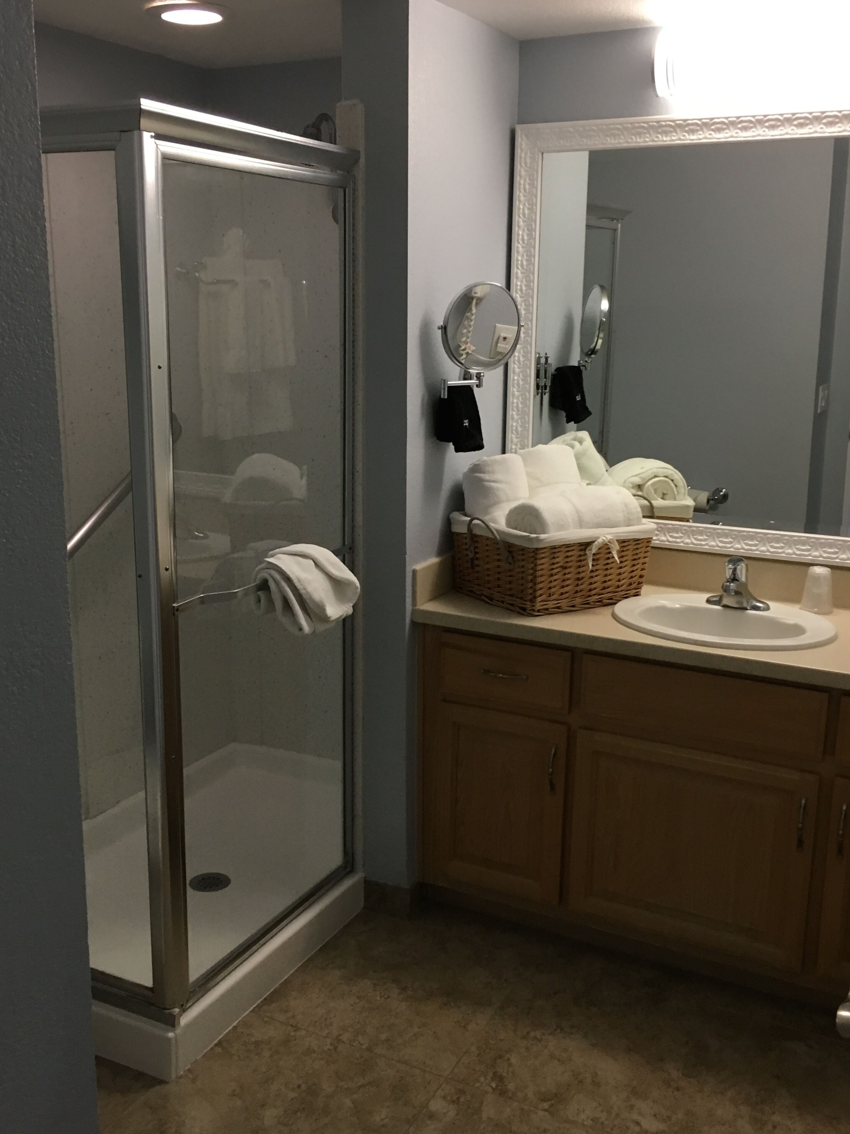 Un baño con ducha envuelta en vidrio, un lavabo con espejo y una cesta de mimbre sobre la encimera.