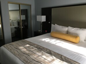 Ein Hotelzimmer mit einem großen Bett, einem Nachttisch mit Lampe, einem Spiegel und einem Kleiderschrank.