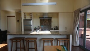 Una cocina moderna con una isla central, taburetes de bar y una puerta corrediza de vidrio que da a un espacio exterior.
