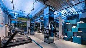 Une salle de sport moderne équipée de tapis de course, de poids et d’une horloge numérique affichant 18h23.