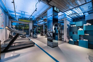Un gimnasio moderno con cintas de correr, pesas y un reloj digital que marca las 18:23.