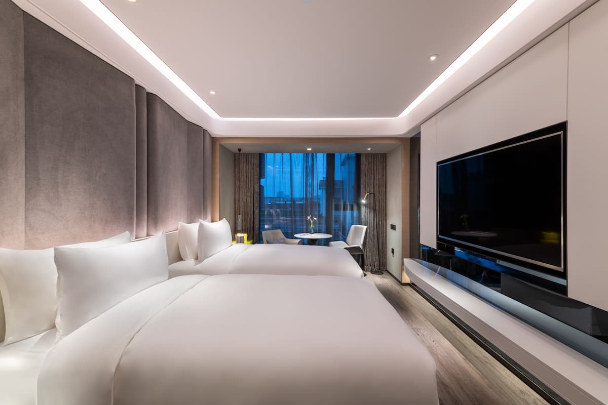 Une chambre d’hôtel moderne dotée d’un grand lit, d’un téléviseur à écran plat, d’une petite table ronde et d’un coin salon avec des fauteuils.