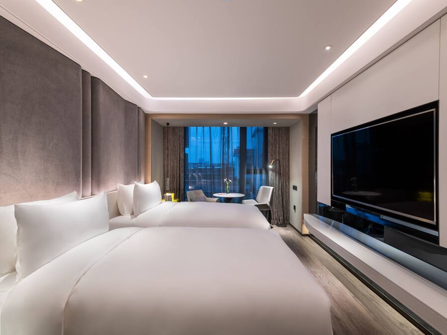 Una habitación de hotel moderna con una cama grande, un televisor de pantalla plana, una pequeña mesa redonda y un rincón de estar con sillas.