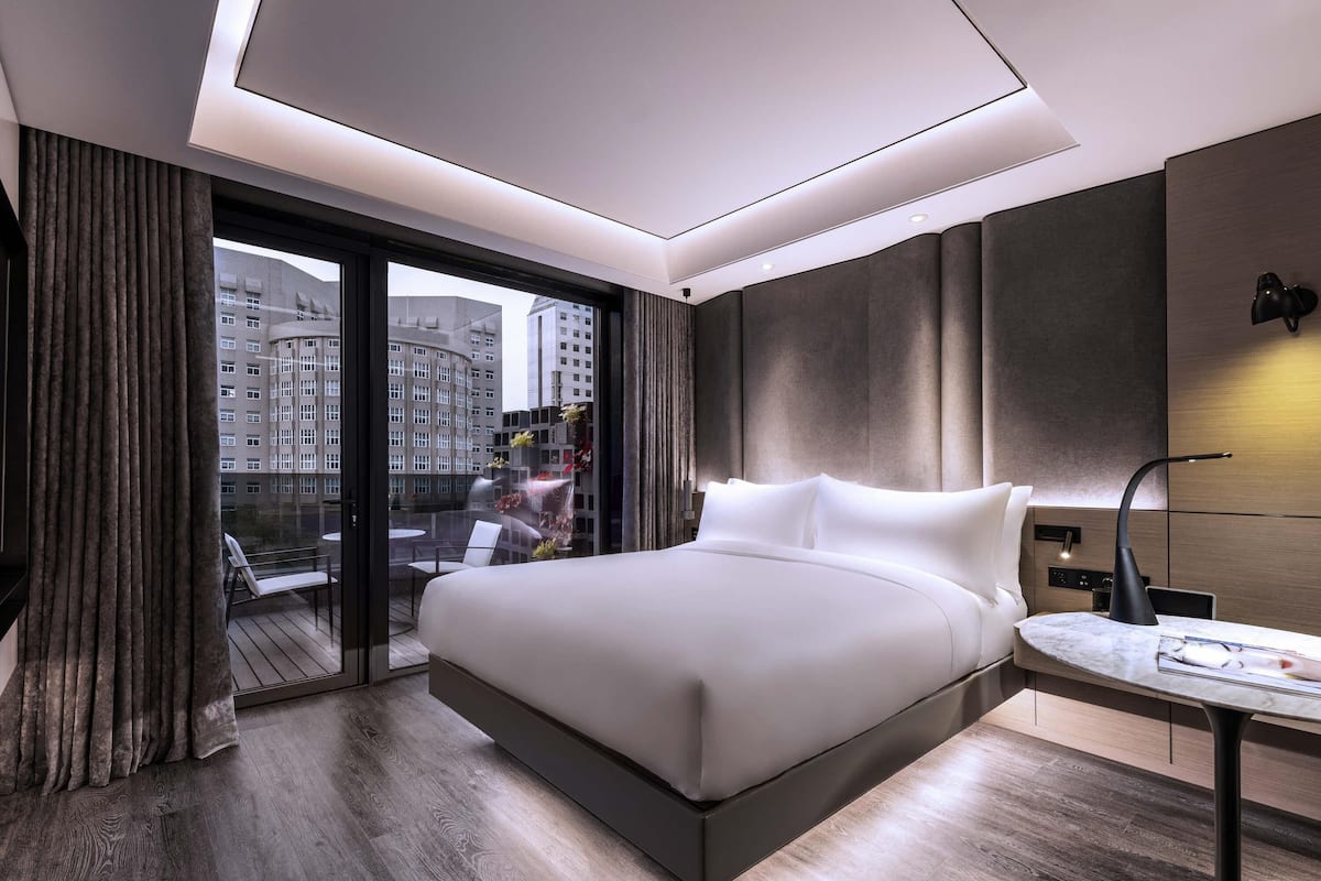 Une chambre d’hôtel moderne, dotée d’un grand lit, d’une petite table et offrant une vue sur le paysage urbain par la fenêtre.