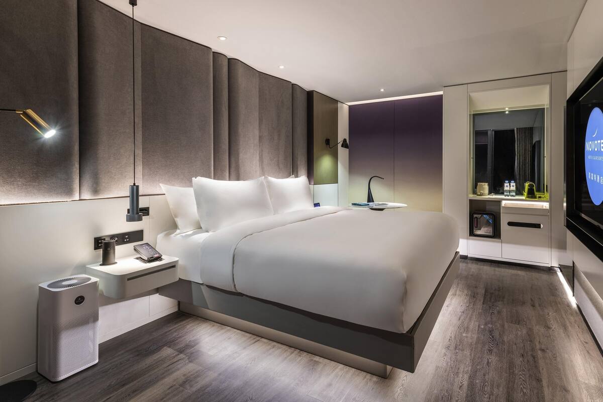 Une chambre d’hôtel moderne avec un grand lit, des tables de chevet, un miroir et un téléviseur intégré.