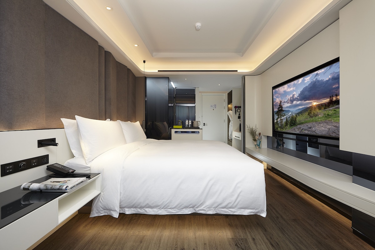 Une chambre d’hôtel moderne dotée d’un grand lit, d’une télévision à écran plat, d’une table de chevet et d’une banquette intégrée.