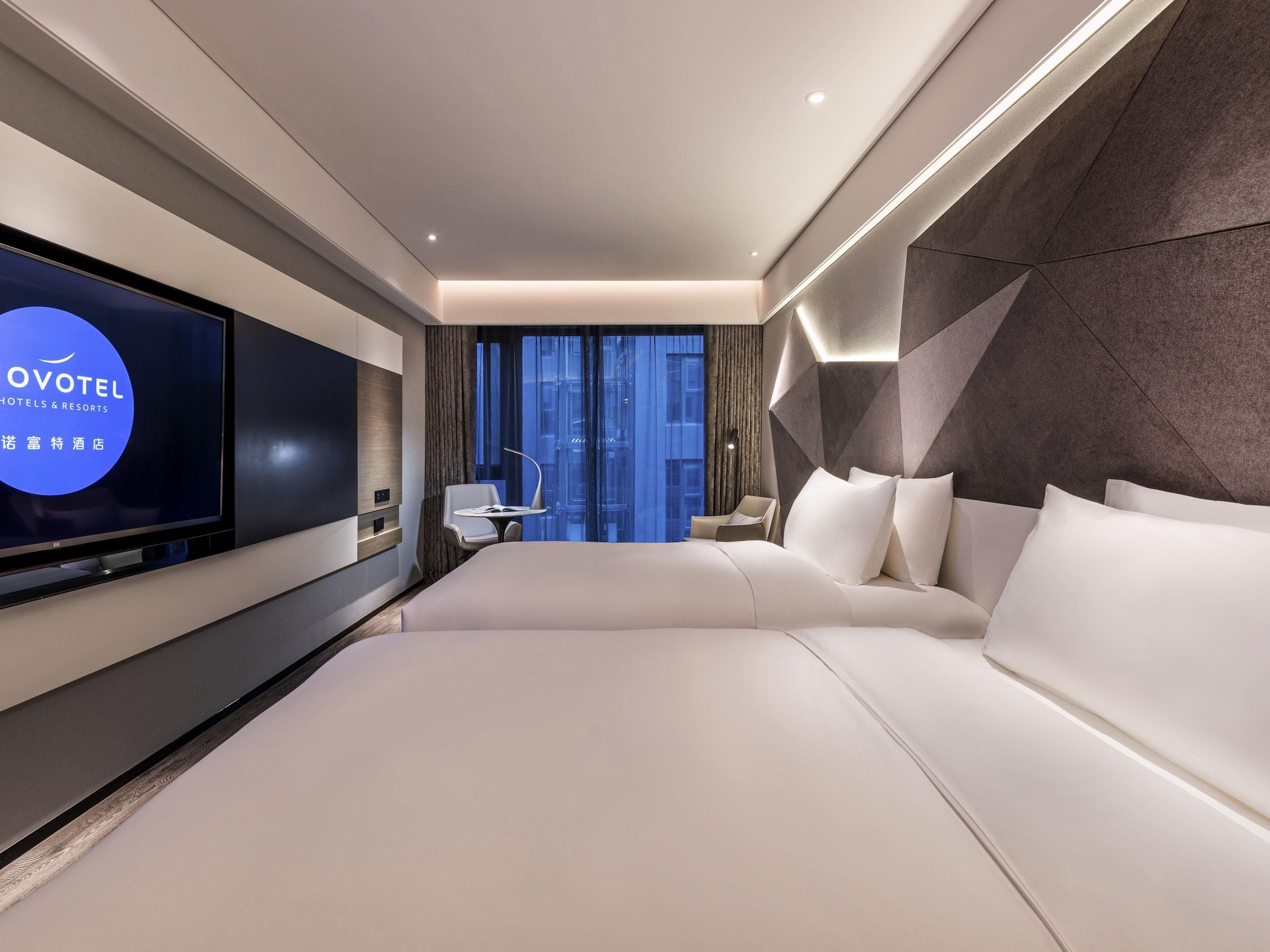 Une chambre d’hôtel moderne avec un grand lit, un téléviseur fixé au mur et une vue sur la ville.