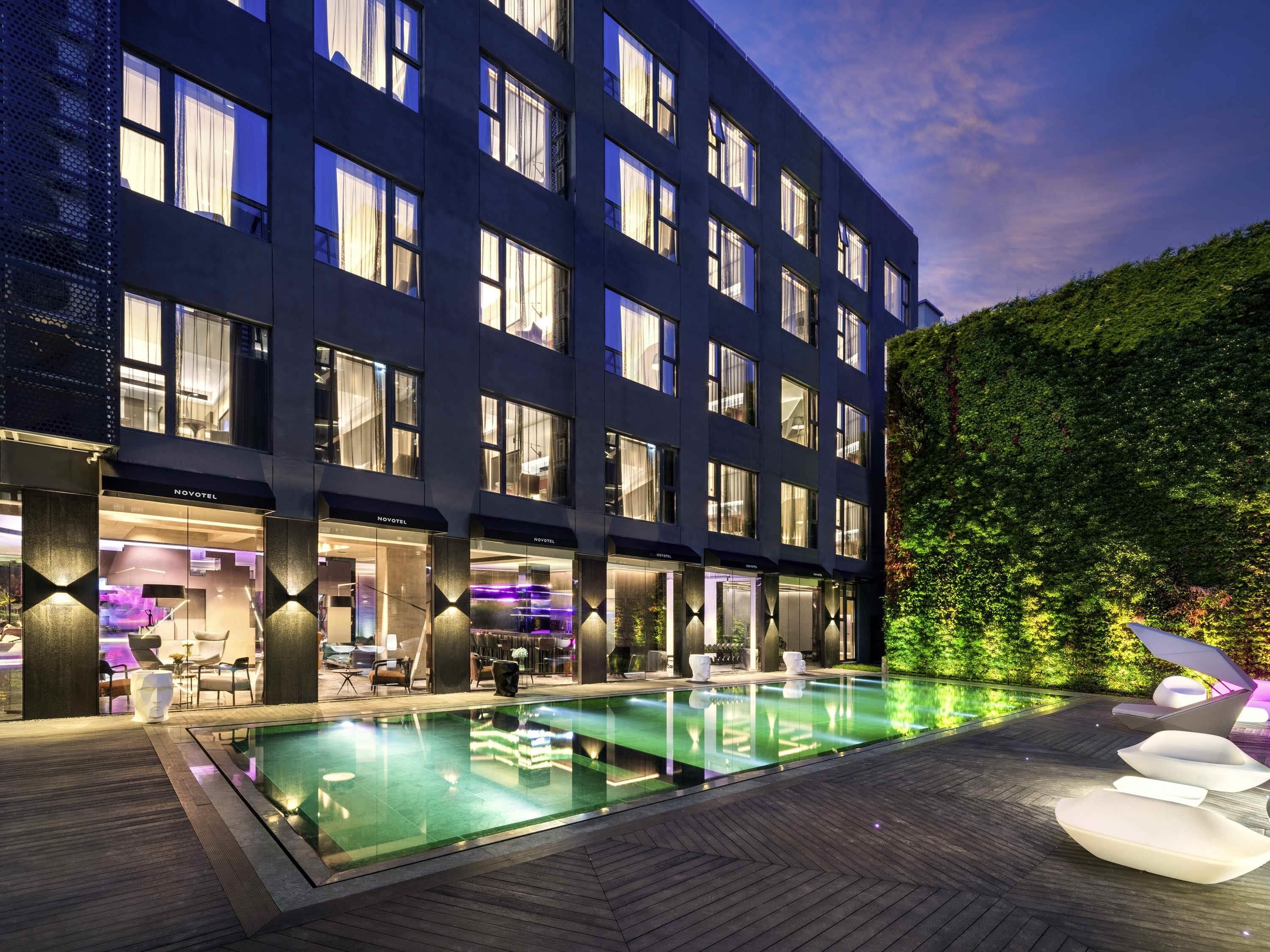Un hotel moderno con piscina, mobiliario exterior y una fachada bien iluminada.