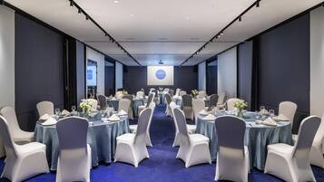 A conference room with round tables, white chairs, and a blue carpet.