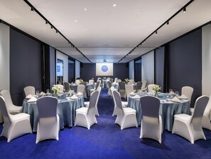 A conference room with round tables, white chairs, and a blue carpet.