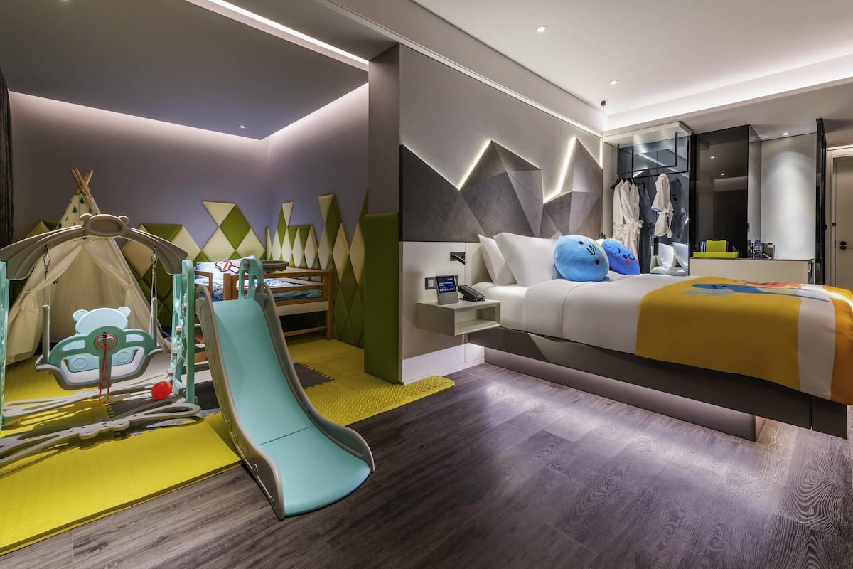 Une chambre d’hôtel moderne équipée d’un lit, d’un bureau, d’une chaise, d’un espace de jeux et d’une armoire.