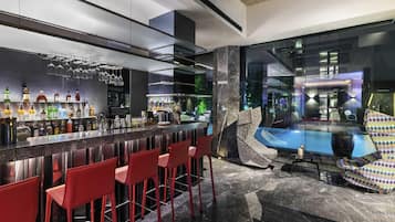 A modern bar area with a marble countertop, red bar stools, and a pool view.