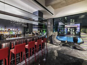 A modern bar area with a marble countertop, red bar stools, and a pool view.