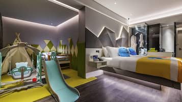 A modern hotel room with a bed, a desk, a chair, a play area, and a wardrobe.