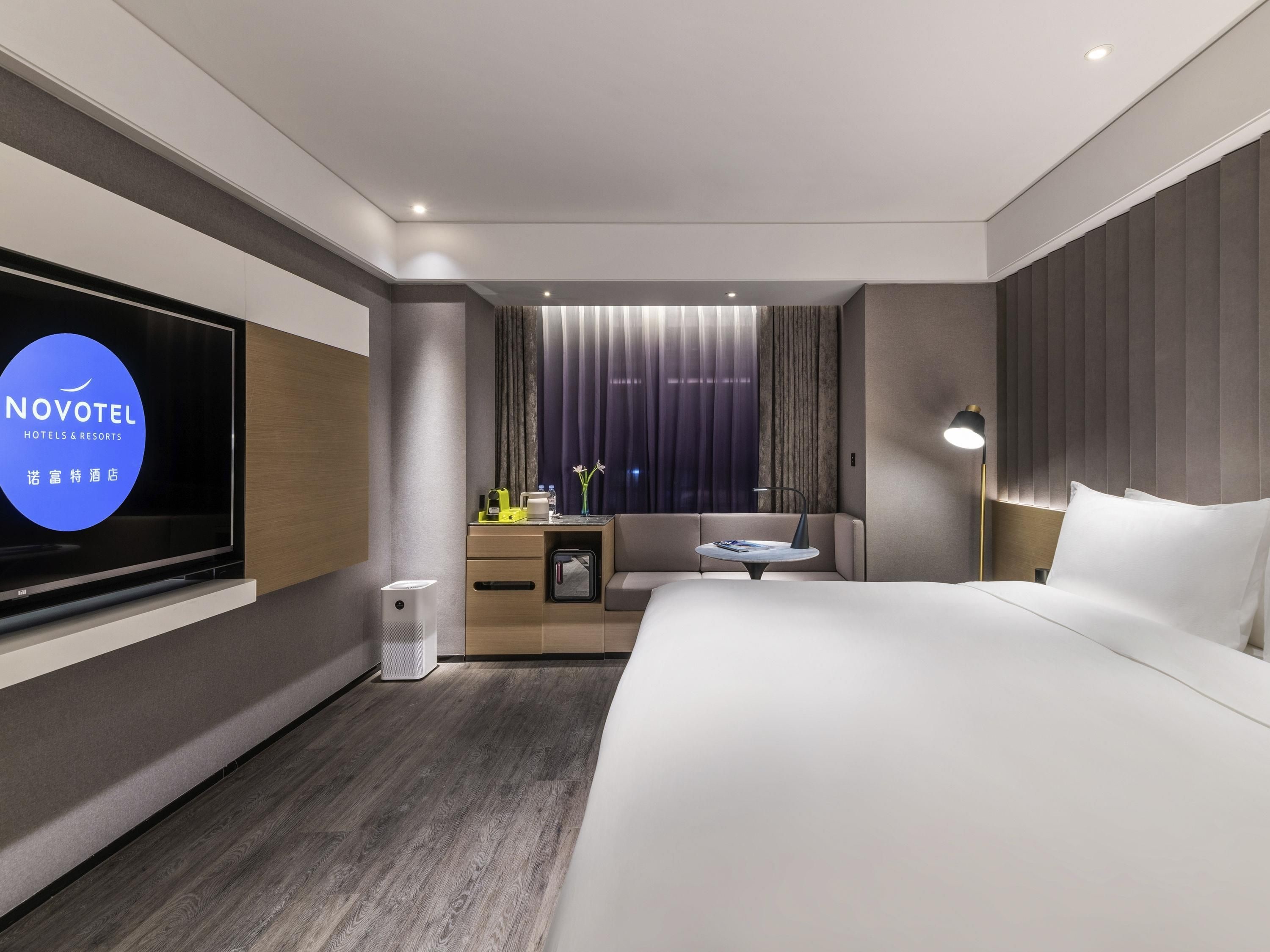 Una habitación de hotel moderna con una cama grande, televisión, una mesita, un sofá y un escritorio con lámpara.
