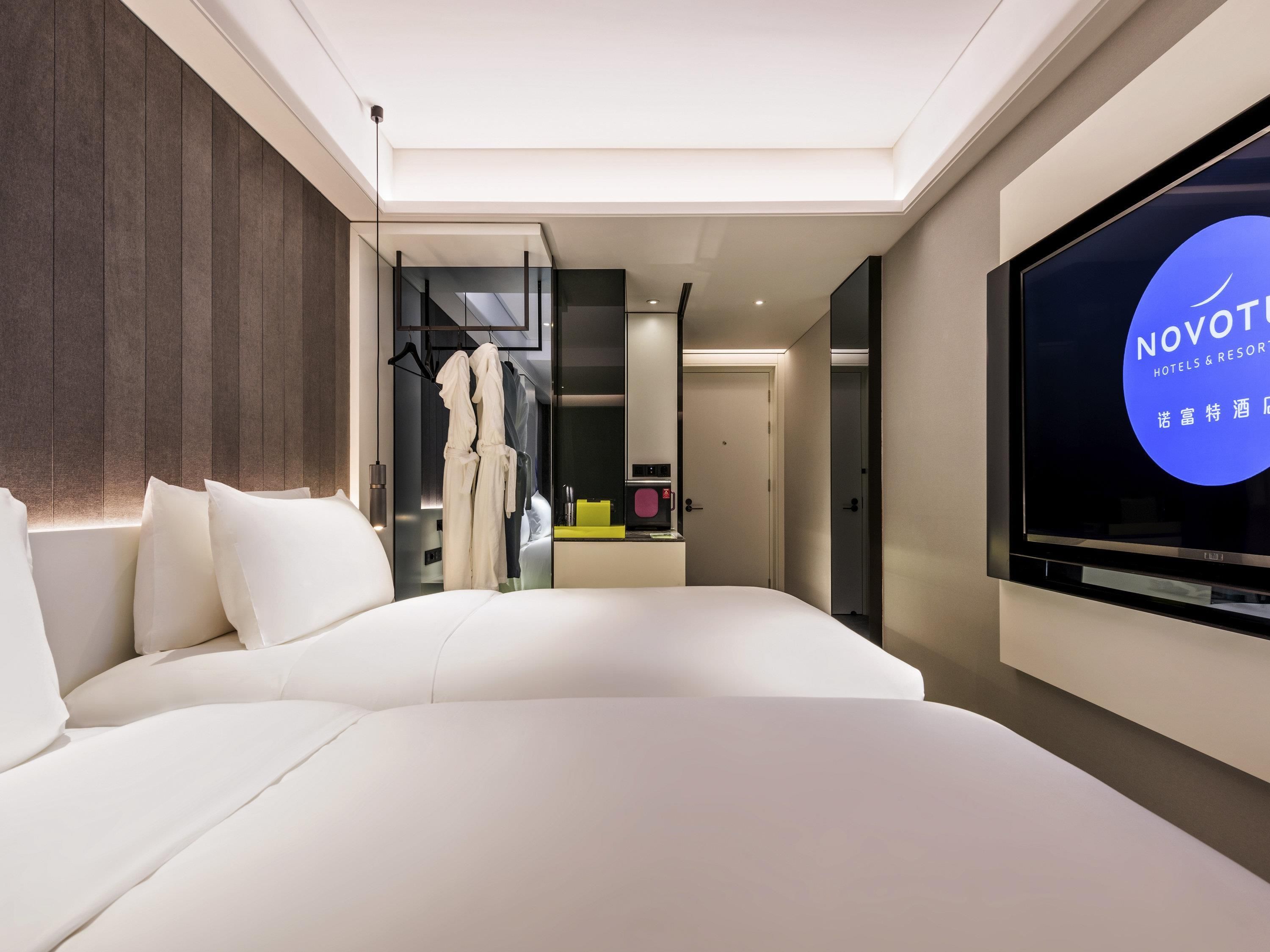 A modern hotel room with a large bed, a TV screen displaying the Novot hotel logo, and a walk-in closet.