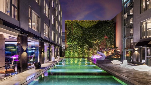 Een modern hotelinterieur met een centraal gelegen zwembad, zithoeken en een weelderige verticale tuinwand.