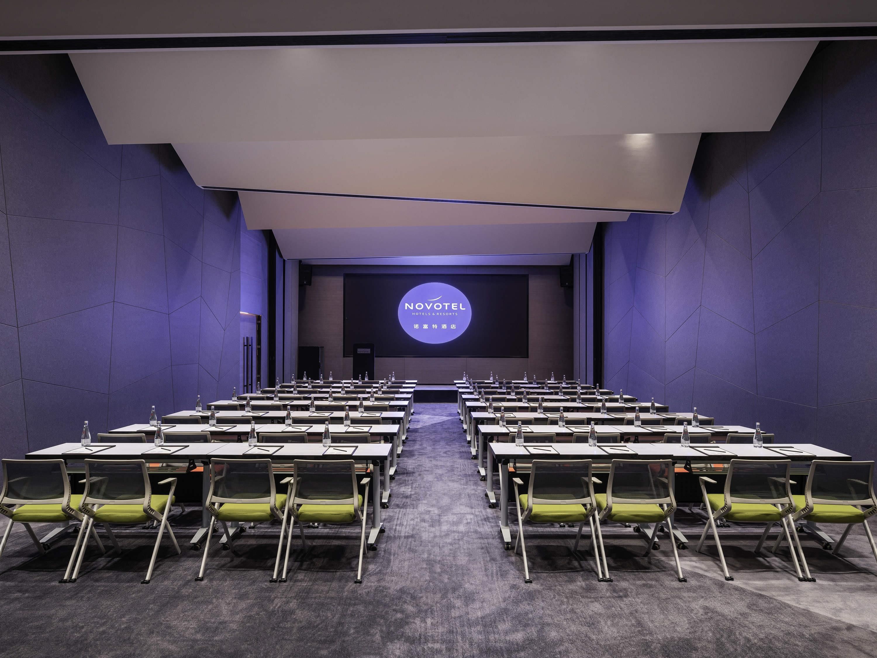 A conference room with rows of tables and chairs, a large screen at the front, and a modern design.