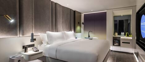 Una habitación de hotel moderna con una cama grande, mesitas de noche, un espejo y televisión integrada.