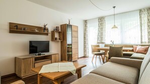 Een moderne woonkamer met een bank, televisie, houten kasten en een eethoek met een tafel en stoelen.