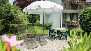 Eine Terrasse mit Gartenmöbeln, einem weißen Sonnenschirm und Blick auf ein Gebäude mit einem Balkon.