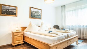 Ein ordentlich bezogenes Bett mit weißer Bettwäsche, ein Nachttisch aus Holz mit einer Lampe und zwei gerahmte Bilder an der Wand.